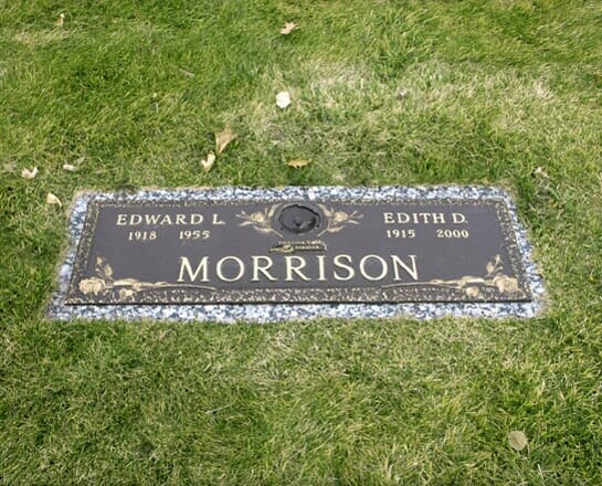 A bronze flush marker mounted on a granite border, set in cemetery grass