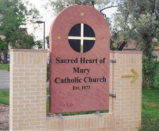 A red sandstone church sign with a gilded cross set into a brick surround