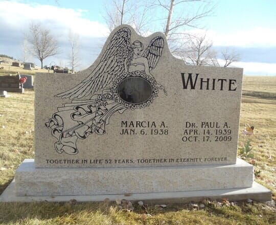 Light granite upright with an etched angel and an oval portrait, standing in a plains cemetery